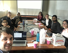 group of people at a table with a box of donuts in front of them