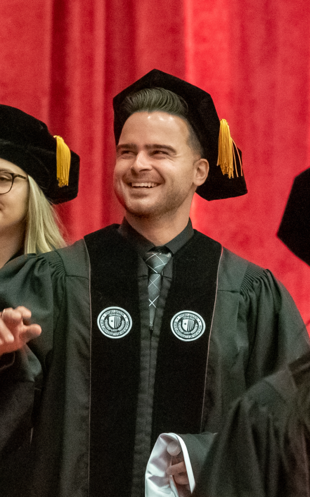 James Vassallo, MD "Person wearing academic regalia standing in front of a red curtain."