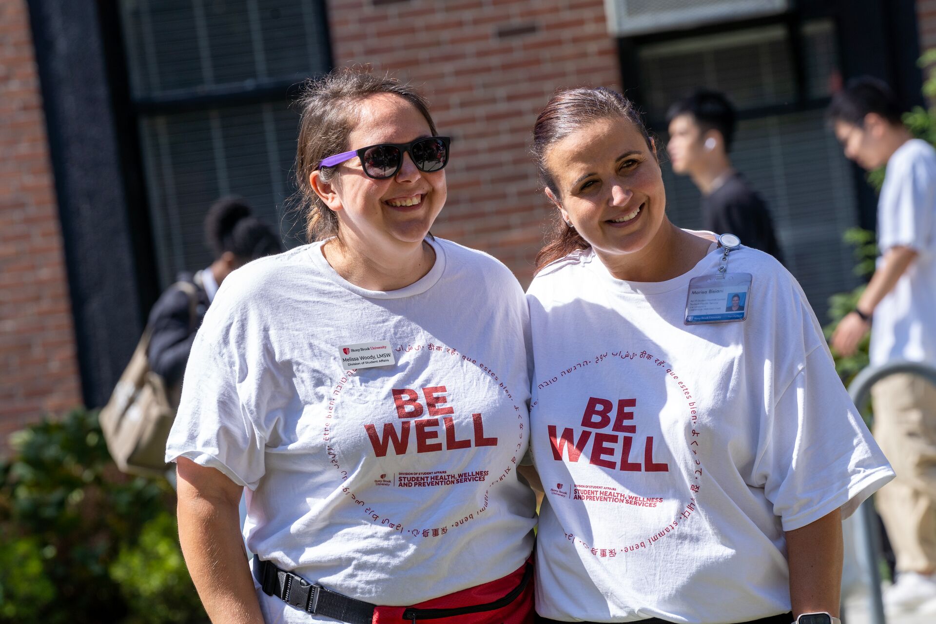 Two female students standing together and smiling at an outdoor wellness event.