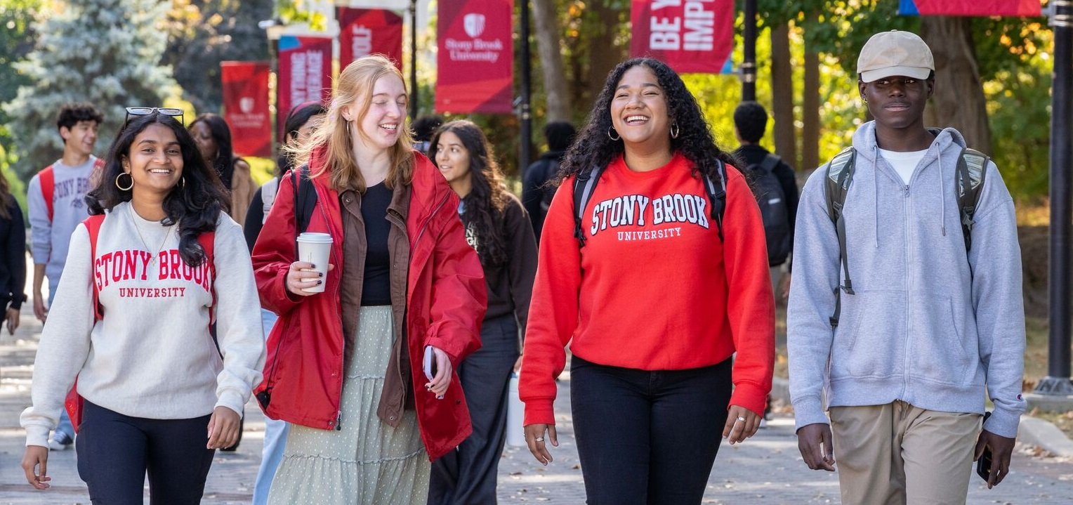 Four college students smiling and walking outside around campus.