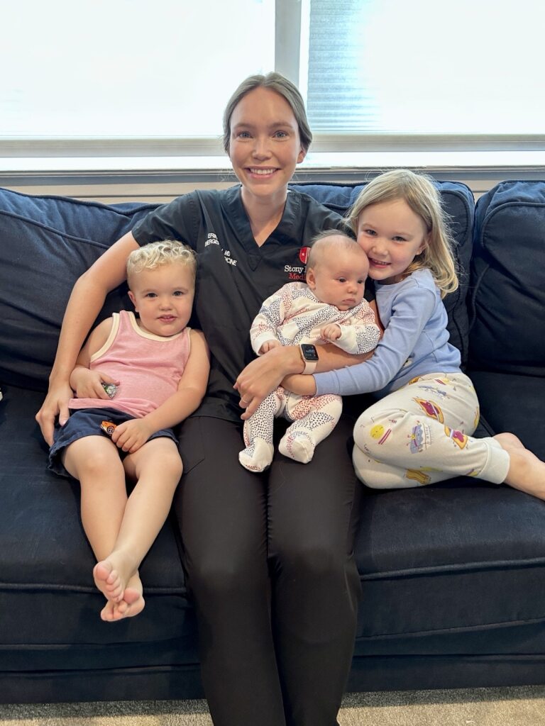 Erin Lavin, MD "Four people sitting on a dark blue couch, including a baby and two children, with a window and blinds in the background."