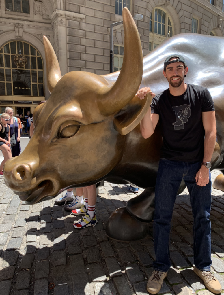 Michael Robison, DO "Person standing next to the Charging Bull statue in New York City, with buildings and other people in the background."