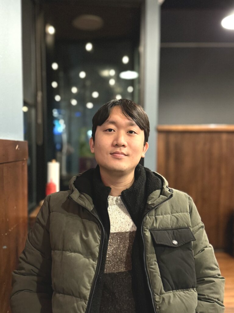 Christopher Loh, MD "Person sitting indoors in a restaurant or café with wooden paneling and a glass door in the background.