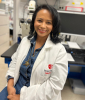 Image of Dr. Acosta smiling at camera while seated in lab wearing lab coat